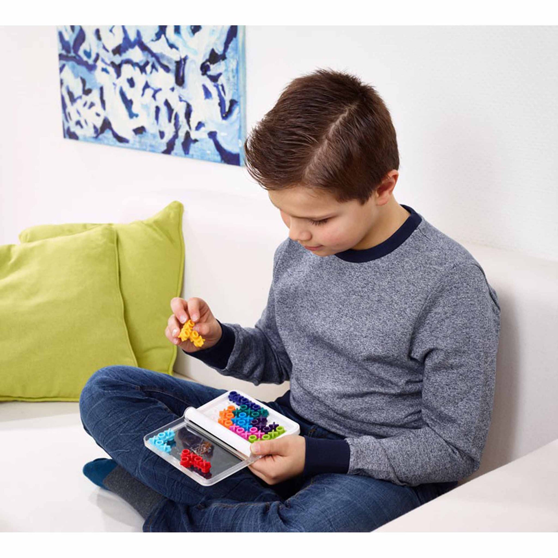 Photo of a boy sitting cross-legged on a couch playing IQ XOXO mind puzzle by Smart Games.