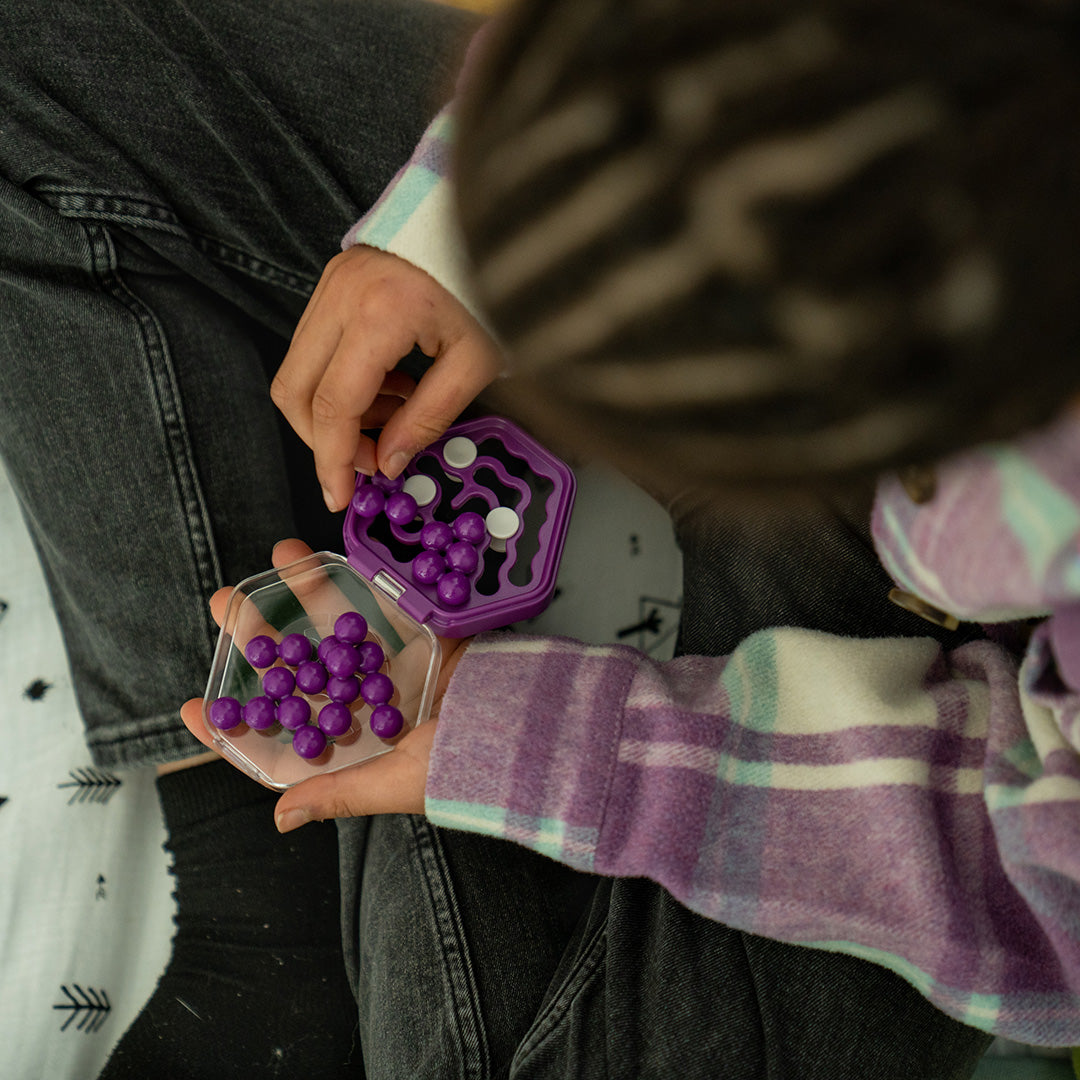 Top down photo of someone playing a purple version of IQ Mini Hexpert mind puzzle by Smart Games.